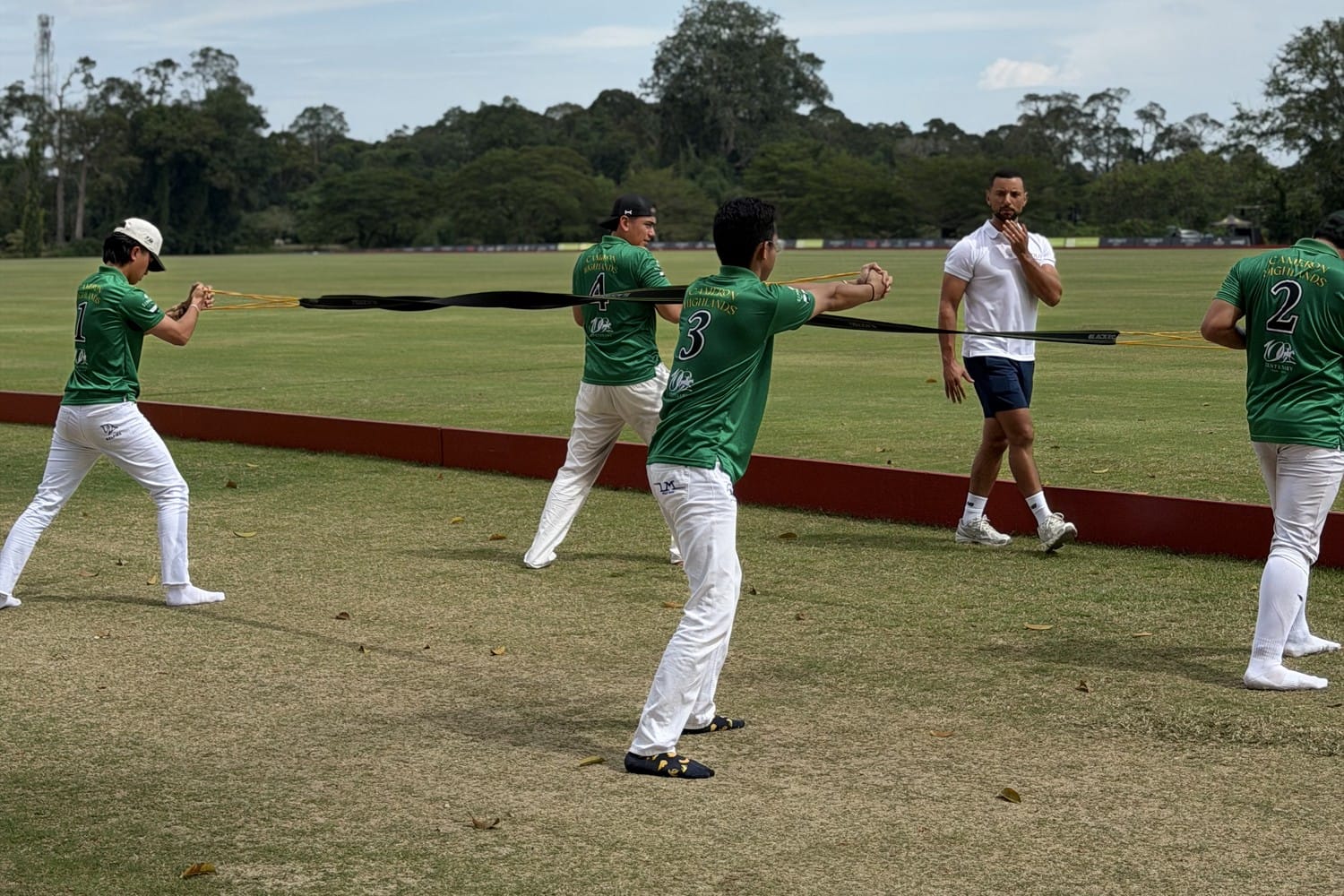 Polo players performing a resistance-band warm-up with their coach on the polo field